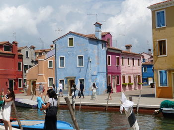 People on canal by buildings against sky