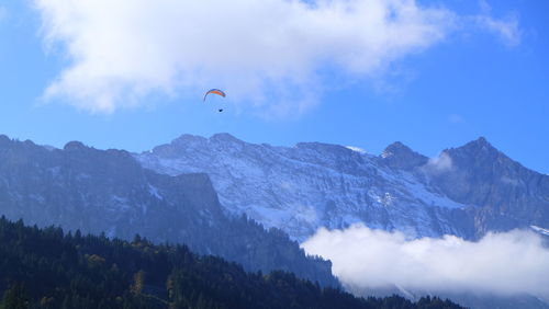 Low angle view of paraglider flying over mountains against blue sky