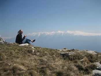 Side view full length of woman sitting against snowcapped mountains