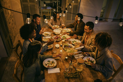 High angle view of smiling friends sitting at illuminated dining table during dinner party