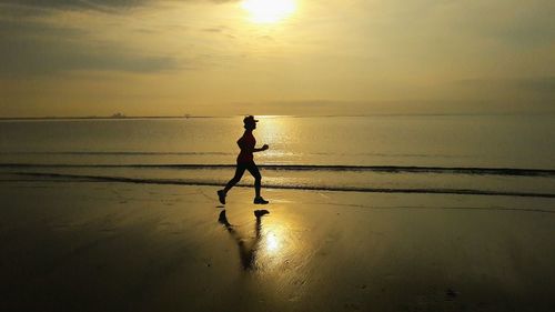 Silhouette man standing on beach against sky during sunset