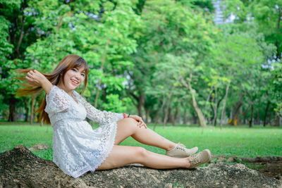 Young woman sitting on plant against trees