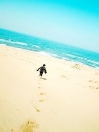 Rear view of mid adult man with backpack walking at beach against clear sky during sunny day