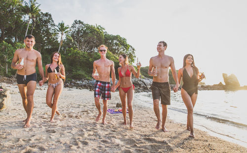 Friends walking with beer bottles at beach