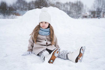 Cute girl sitting on snow covered landscape during winter