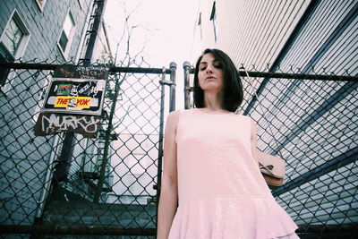 Low angle view of mid adult woman standing against chainlink fence