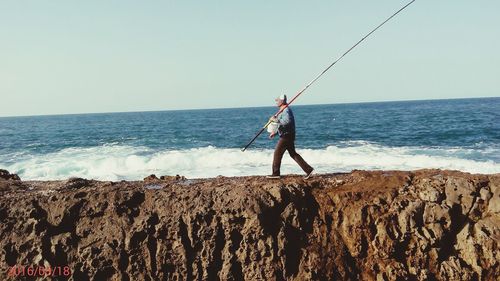 Man fishing at sea against clear sky