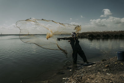 Man fishing in lake against sky