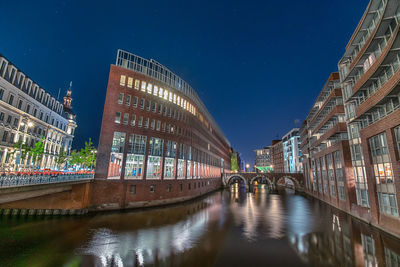 Bridge over canal amidst buildings in city at night