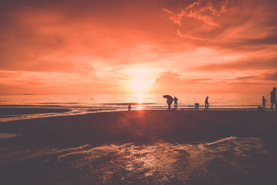 Silhouette people standing on beach against orange sky