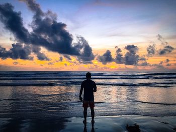 Rear view of silhouette man standing at beach during sunset