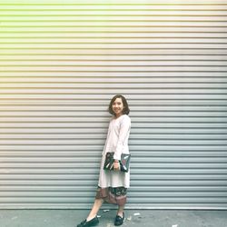 Full length side view of smiling woman standing against shutter