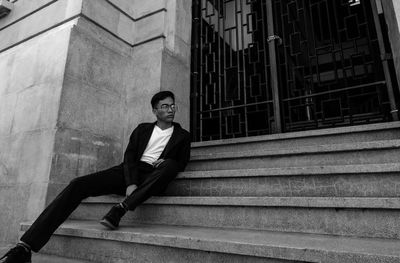 Full length of thoughtful young man looking away while sitting on staircase