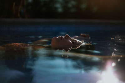 Side view of face above water surface of resting tranquil woman with closed eyes in swimming pool on sunny summer day