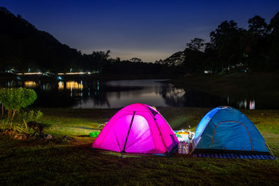 Multi colored tent on grass by lake against sky