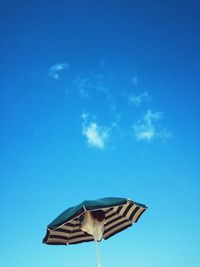 Low angle view of blue sky with striped sun-shading umbrella