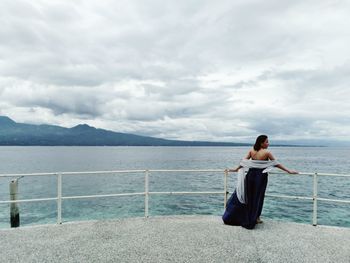 Rear view of woman sitting on shore against sky