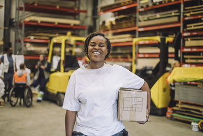 Portrait of happy carpenter with cardboard box at warehouse