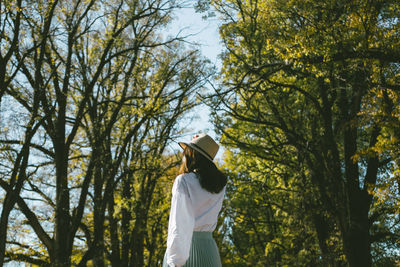 Rear view of young woman standing against trees in park during sunny day