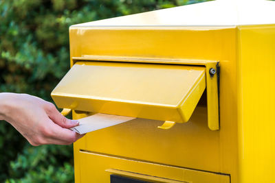 Cropped hand inserting envelope in yellow public mailbox