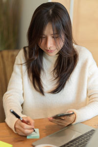 Mid adult woman using mobile phone while sitting on table