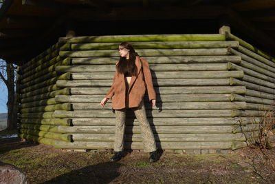 A young woman with a brown coat, posing in front of old wooden planks