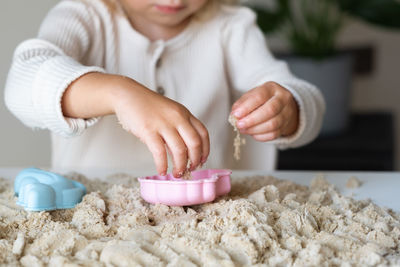 Blonde,curly-haired toddler,baby girl playing with kinetic sand indoors.motor skill, sensorics