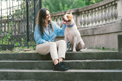 Woman sitting on stone staircase and patting american pitbull terrier. happy dog looking at owner