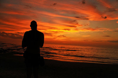 Rear view of silhouette man standing at beach during sunset