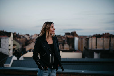 Young woman standing against cityscape during sunset
