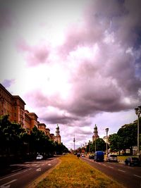 Road passing through city against cloudy sky