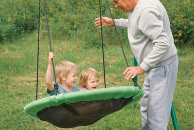 Grandfather swinging children in summer park. grand dad and grandchildren sitting on swing outdoors