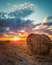 Hay bales on field against sky during sunset