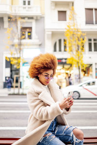 Young woman using mobile phone while sitting in city