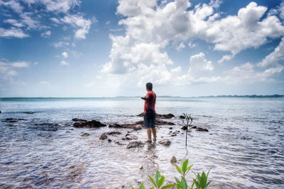 Rear view of man standing on beach against sky