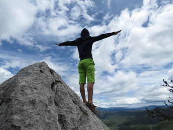 Low angle view of woman standing on rock against sky