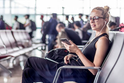 Smiling woman using smart phone sitting at airport