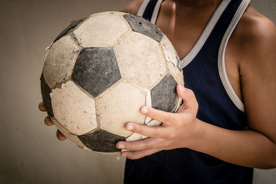 Midsection of boy standing with soccer ball against wall