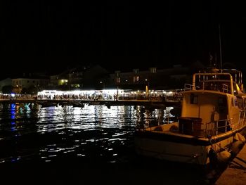 Boats moored at illuminated harbor against sky at night