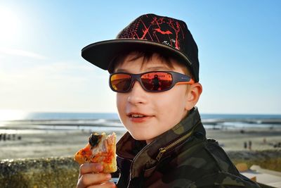 Portrait of boy eating pizza and wearing sunglasses against sea