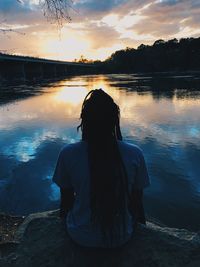 Rear view of silhouette man sitting on shore against sunset sky