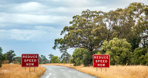 Road sign by trees against sky