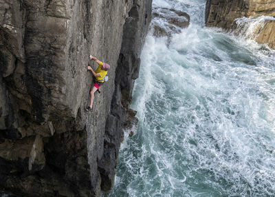 Mature male rock climber climbing up cliff against sea