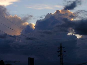 Low angle view of electricity pylon against cloudy sky