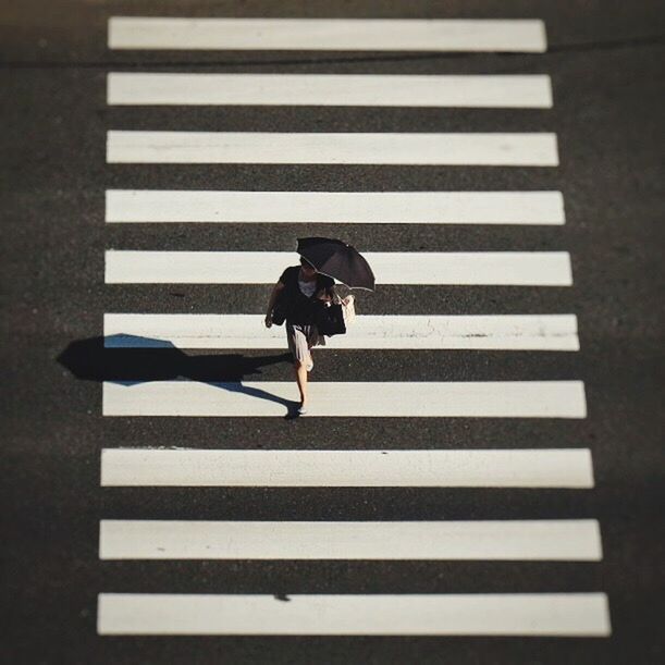 HIGH ANGLE VIEW OF WOMAN WALKING ON ZEBRA CROSSING ON ROAD