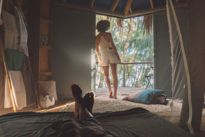 Low section of man lying on bed while woman standing at doorway in cottage