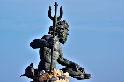 Low angle view of neptune statue against blue sky