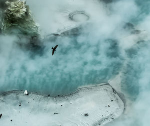 High angle view of bird flying over hot springs with smoke