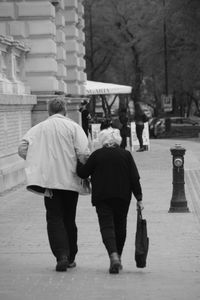 Rear view of people walking on sidewalk in city