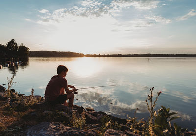 Adolescent boy fishing on shore of lake at sunset in ontario, canada.